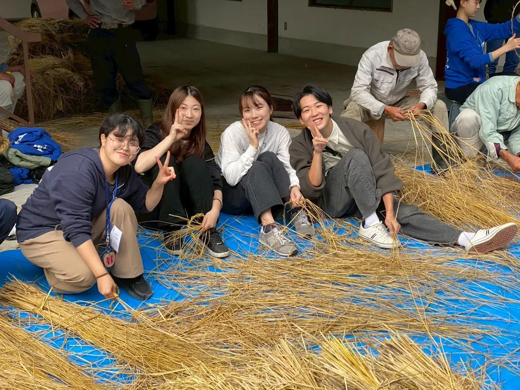 しめ縄づくりの合間に、わらの上に並んで座る人たち