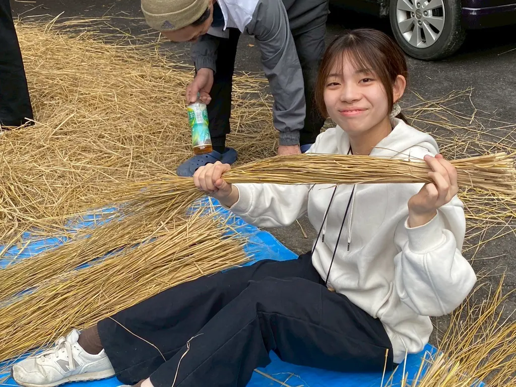 しめ縄に使う稲わらの束を広げて、笑う女性