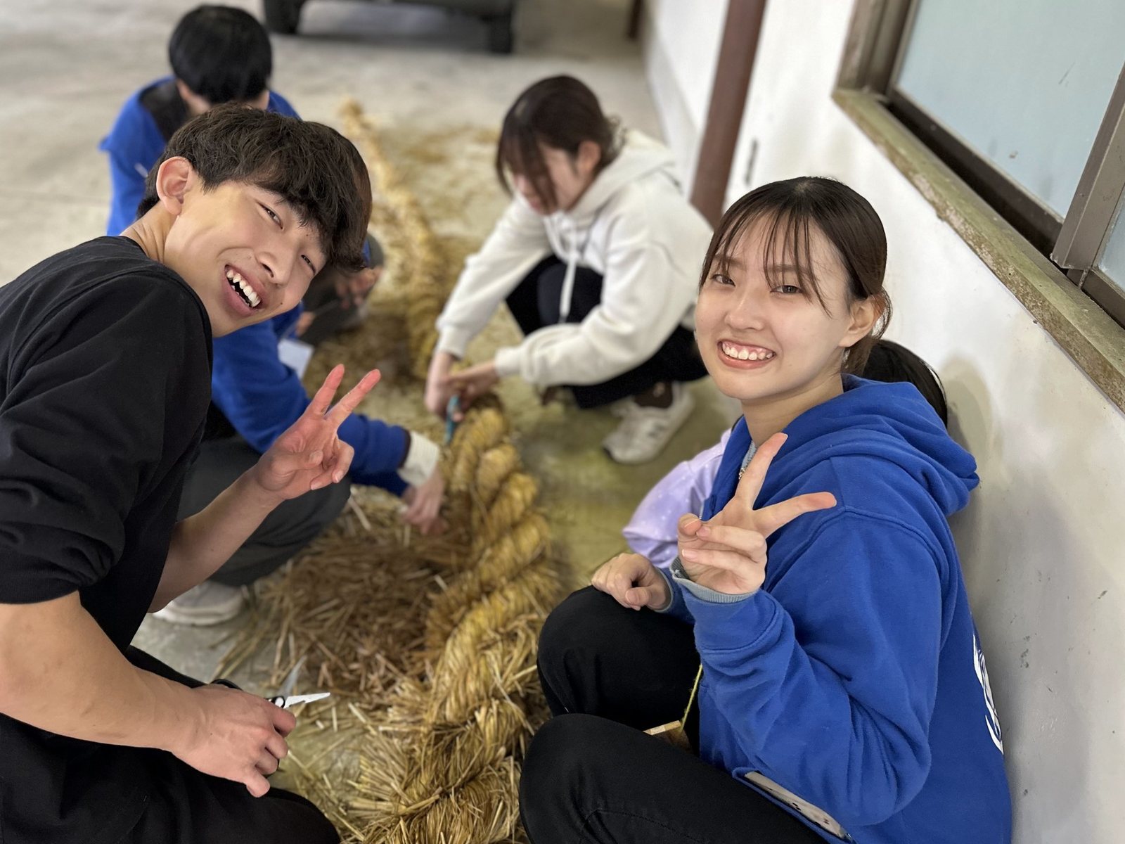 しめ縄をないながら笑顔でピースする若者たち