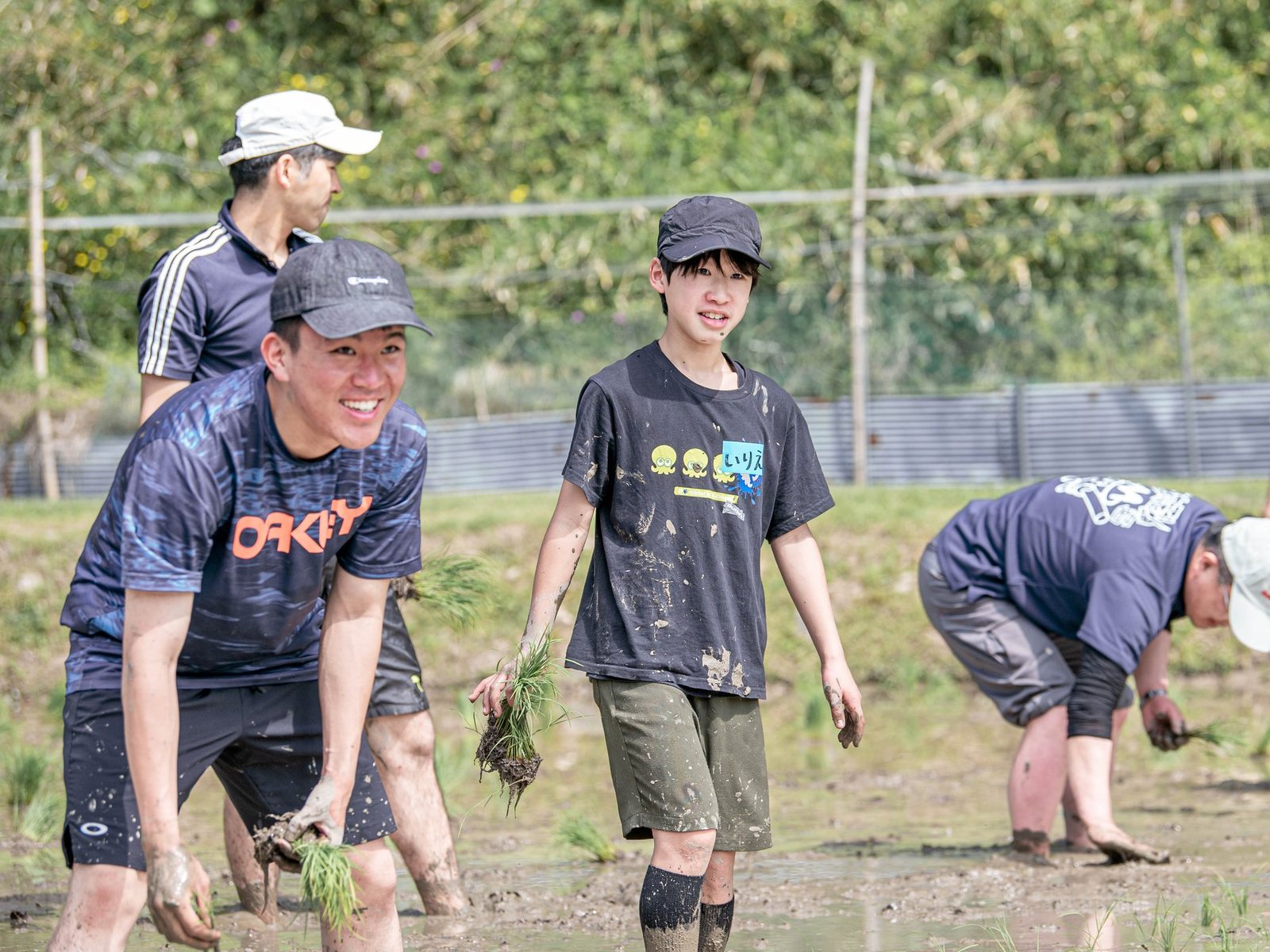 田んぼに入り、苗を手に笑顔で田植えをする若者たち
